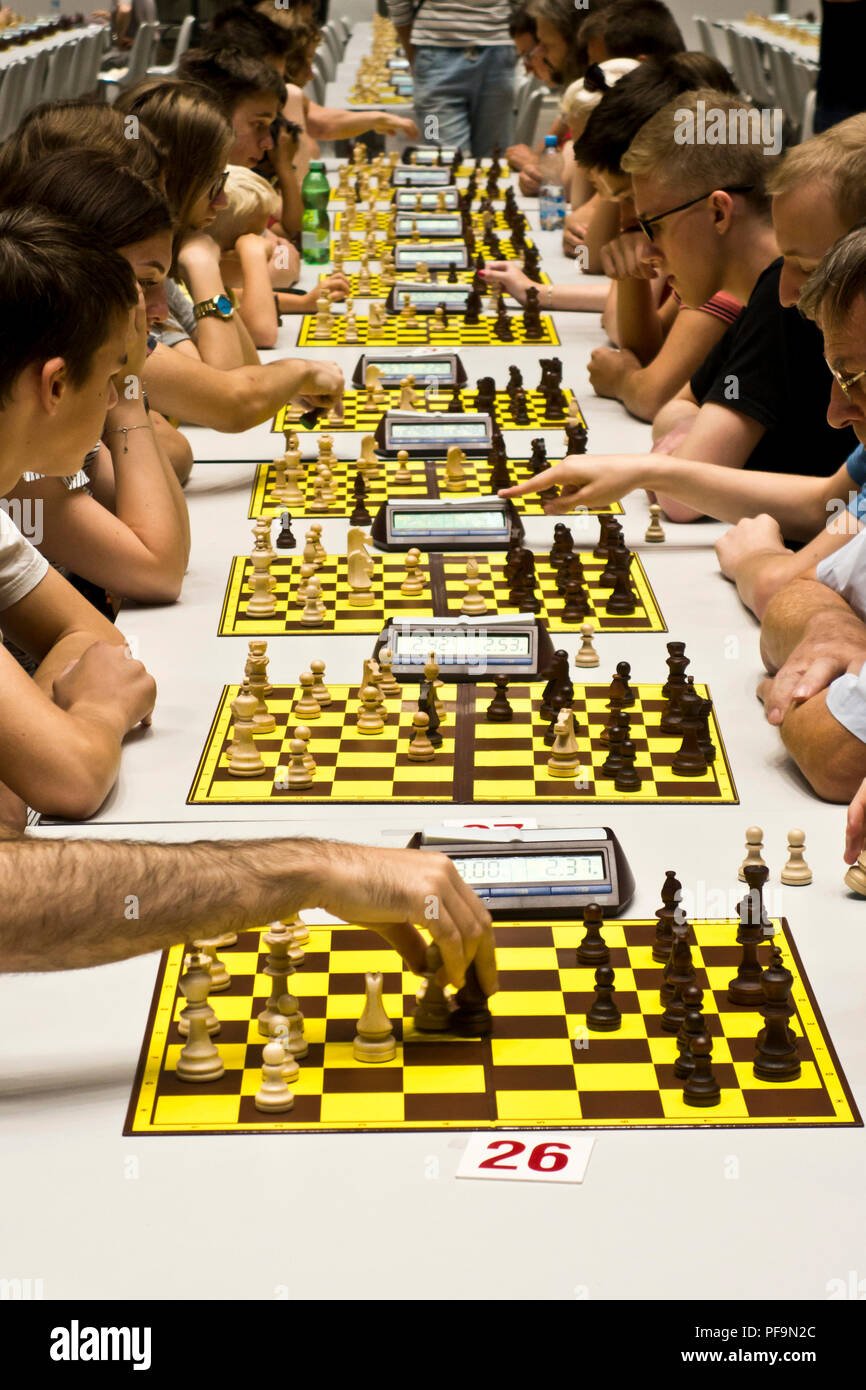 Les joueurs s'affrontent sur plusieurs plateaux lors d'un tournoi d'échecs indoor bondé, utilisant des horloges numériques dans une grande salle Banque D'Images