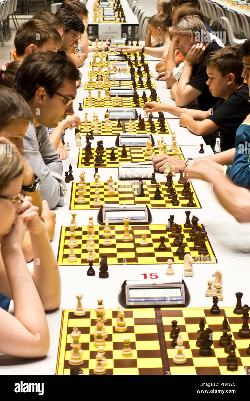 Les joueurs s'affrontent sur plusieurs plateaux lors d'un tournoi d'échecs indoor bondé, utilisant des horloges numériques dans une grande salle Banque D'Images