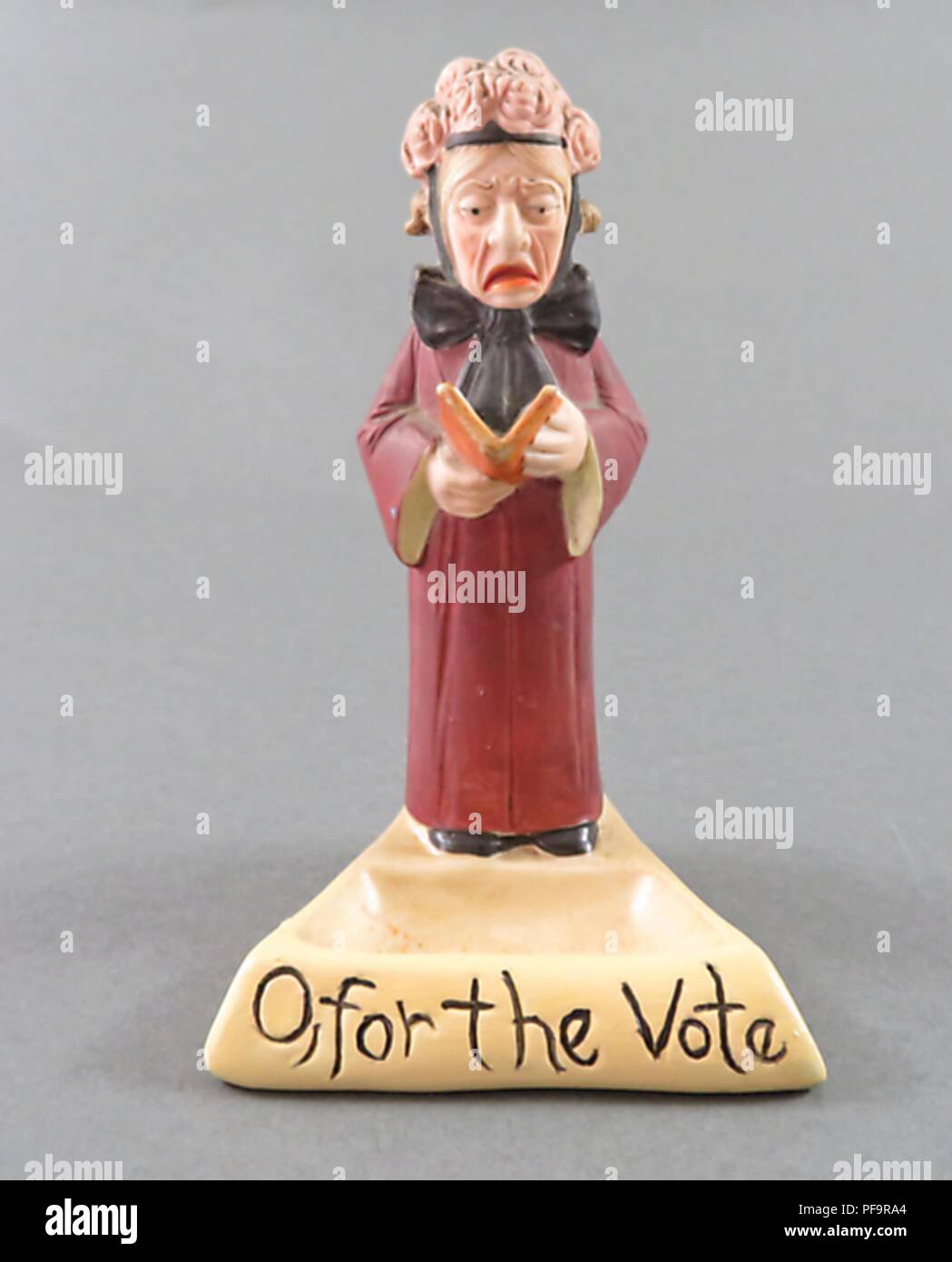 Figurine en céramique représentant une femme plus âgée, debout, portant un chapeau rose orné et un long manteau rouge, et la lecture d'un livre, avec une légende à la base de la figurine qui lit 'O, pour le vote,' produit par l'entreprise allemande de Schafer et Vater tant pour les marchés britannique et américain, 1900. () Banque D'Images