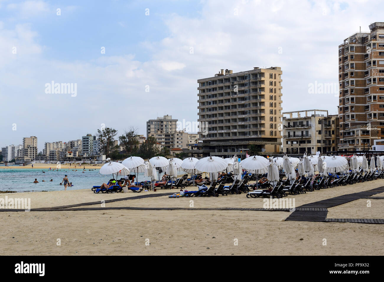 Les touristes sur le Palm Beach à Famagouste (Gazimagusa) avec des blocs d'appartements et hôtels abandonnés en arrière-plan, République turque de Chypre du Nord Banque D'Images