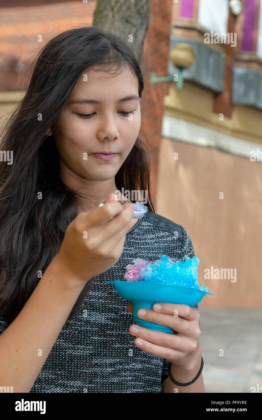 Français/Thaï adolescente avec de longs cheveux noirs mange une caisse noire bleue dans le centre-ville de Warrington Banque D'Images