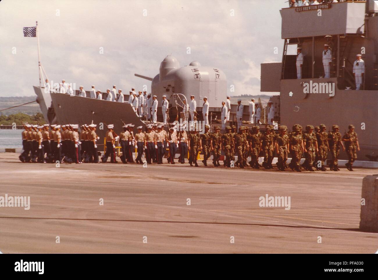 Photographie couleur, montrant plusieurs unités de militaires, y compris les United States Marine Corps (USMC) membres, debout à l'attention sur l'USS Brewton (FF-1086) et marcher sur le quai à proximité, photographié lors de la guerre du Vietnam, 1970. () Banque D'Images