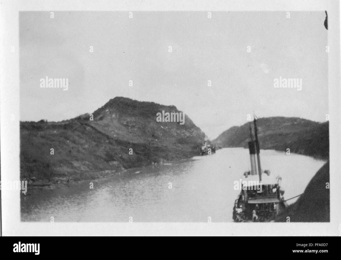 Photographie noir et blanc, tourné à partir d'un pont du navire, montrant un remorqueur le guidage d'un bateau à travers le Canal de Panama, avec des banques centrales visible sur chaque côté, 1915. () Banque D'Images