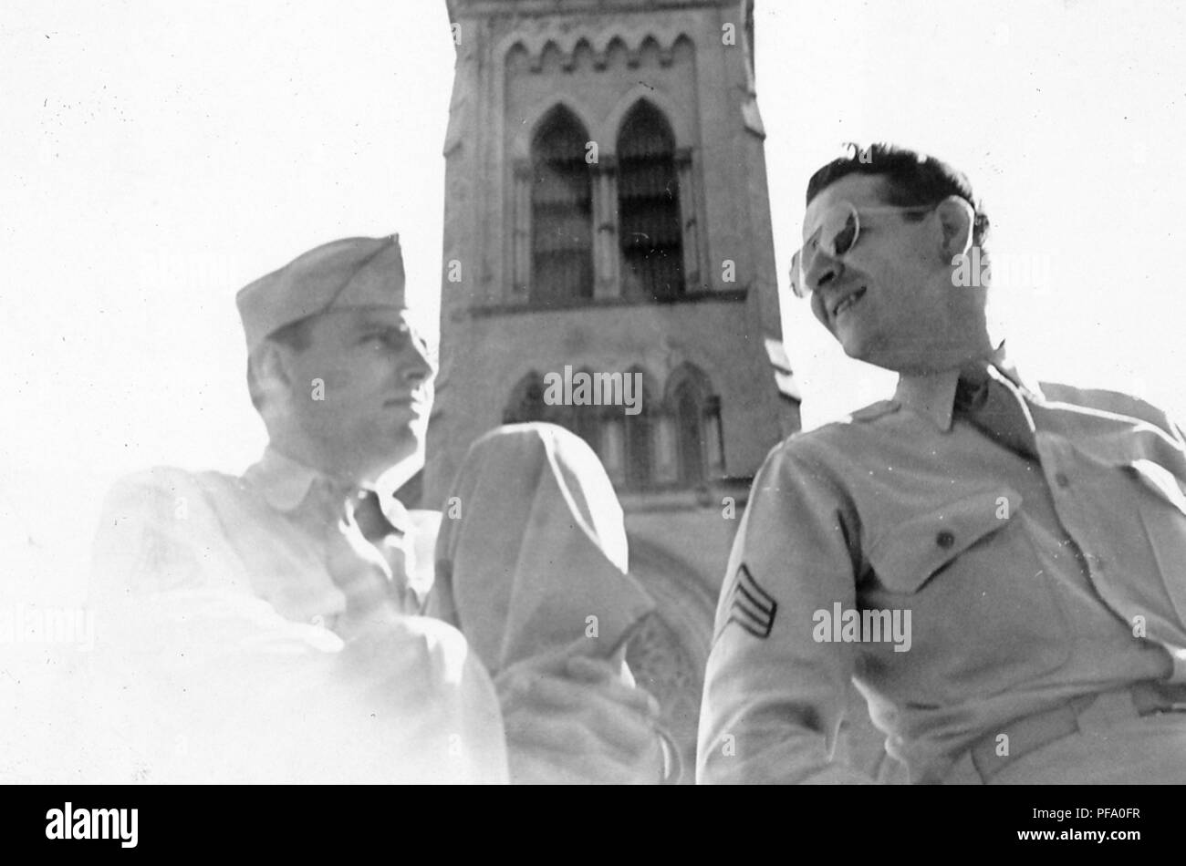 Photographie noir et blanc, tourné à partir d'un angle faible, montrant deux hommes, un militaire en uniforme portant un chapeau, l'autre portant des lunettes, se tourna vers l'autre, avec un Moorish-Revival tower, avec arcs en lancette ou, dans l'arrière-plan, probablement photographié pendant la Seconde Guerre mondiale, 1945. () Banque D'Images