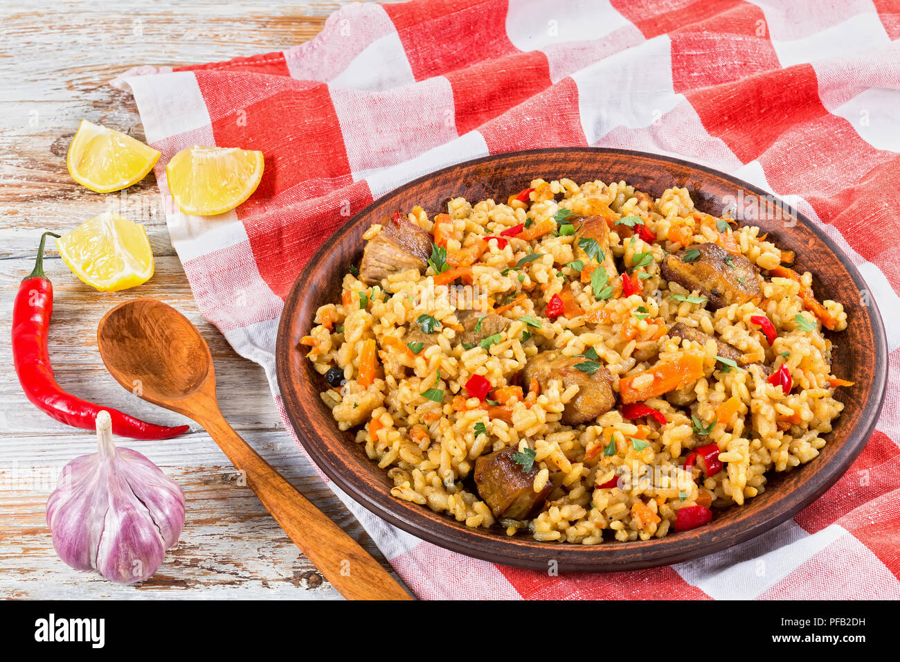 Le riz avec de la viande, le poivre, les légumes et les épices sur le plat d'argile, essuie-tout,tranche de citron, l'Ail, piment et cuillère en bois de la peinture blanche sur pl Banque D'Images