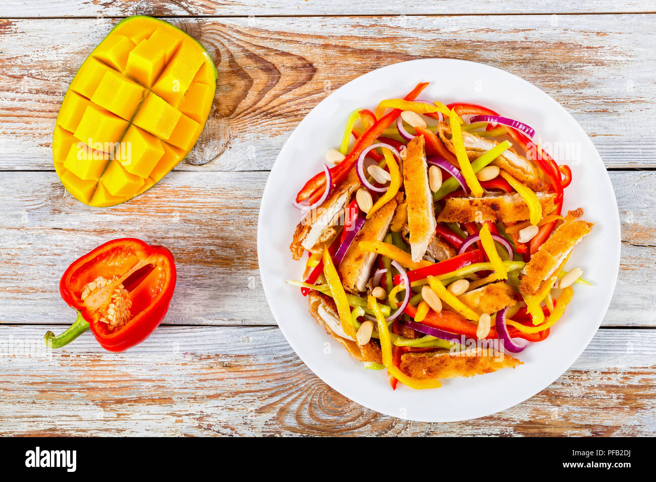 Crumbed pain de viande de poulet, mangue, les arachides, le poivron, l'oignon rouge sur blanc salade plat avec la moitié de la mangue en cubes et le poivron sur blanc p Banque D'Images