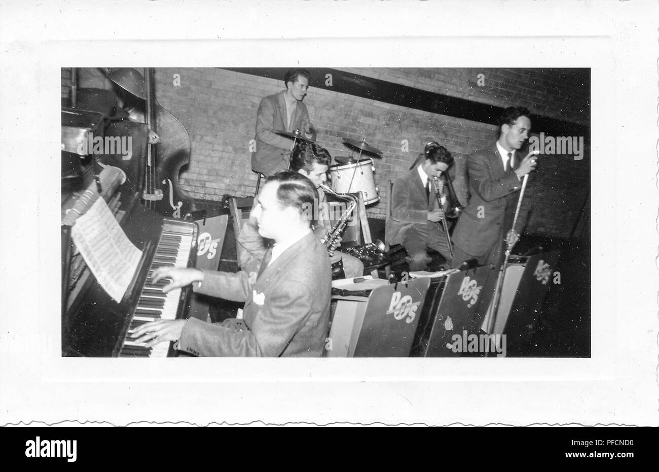 Photographie noir et blanc, montrant un costume-clad cinq homme-orchestre jouant leurs instruments, dont un pianiste, saxophoniste, batteur, et chanteur, avec des logos sur leur matériel à lire 'POS' et un mur de briques visibles dans l'arrière-plan, probablement photographié en Ohio dans la décennie suivant la Seconde Guerre mondiale, 1950. () Banque D'Images