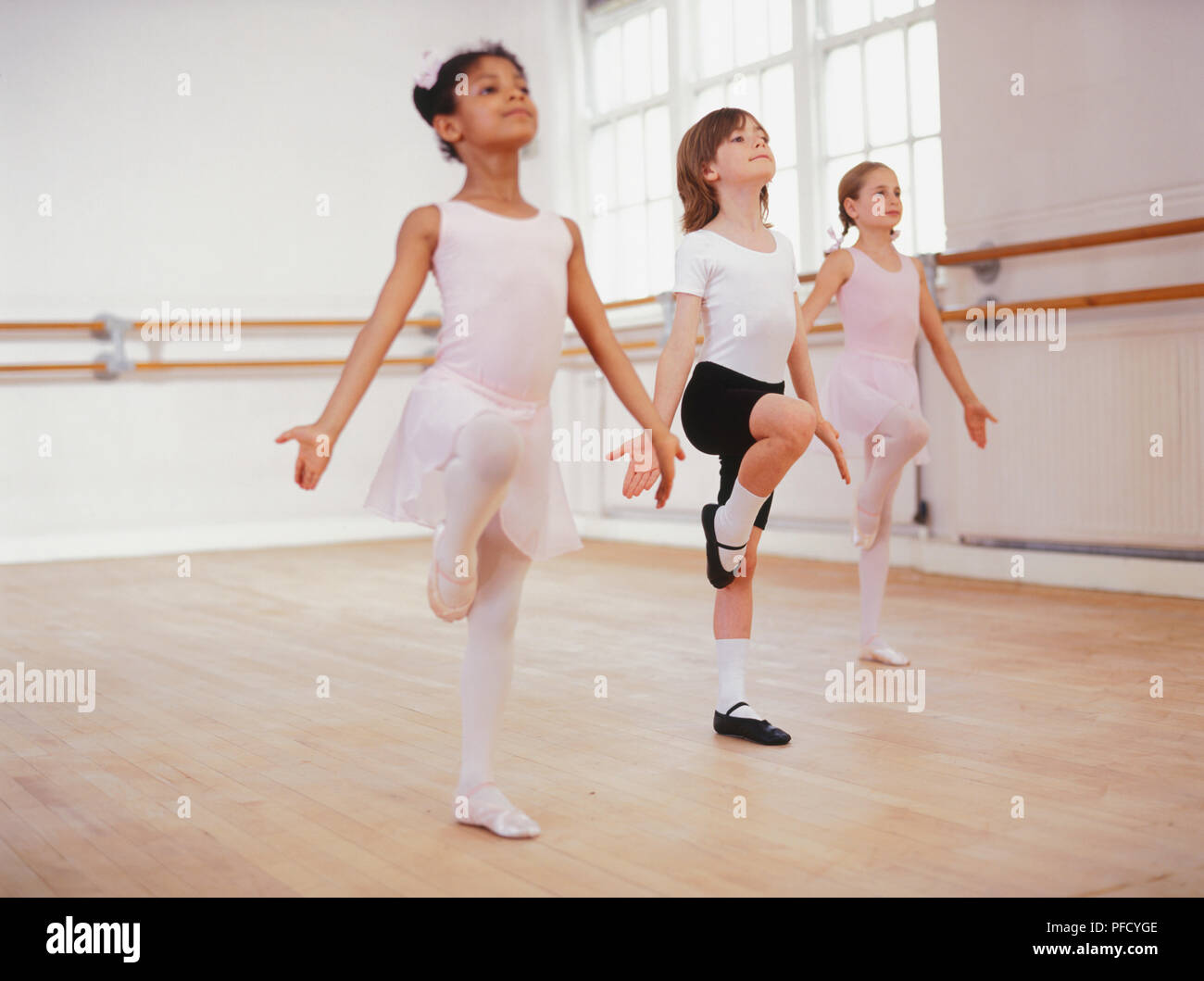 Trois danseurs de ballet dans une classe de ballet, debout avec une jambe levé haut, bras sur le côté les paumes des mains vers l'avant. Banque D'Images