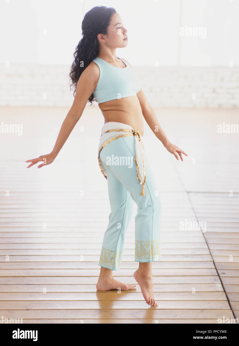 La femme en bleu soutien-gorge de sport et des jambières en faisant un pas en avant, genou légèrement plié et les orteils touchent le sol, les bras légèrement étendu sur le côté, vue de côté. Banque D'Images