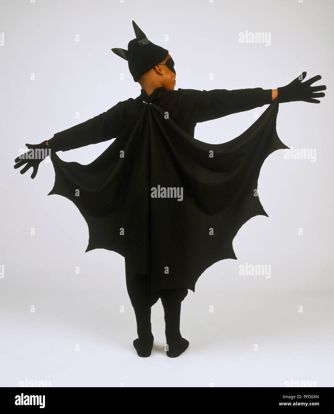 Dark-skinned woman black bat cape, ni bords irréguliers, un chapeau avec des oreilles pointues et des gants, les bras tendus, montrant le cap, vue arrière Banque D'Images
