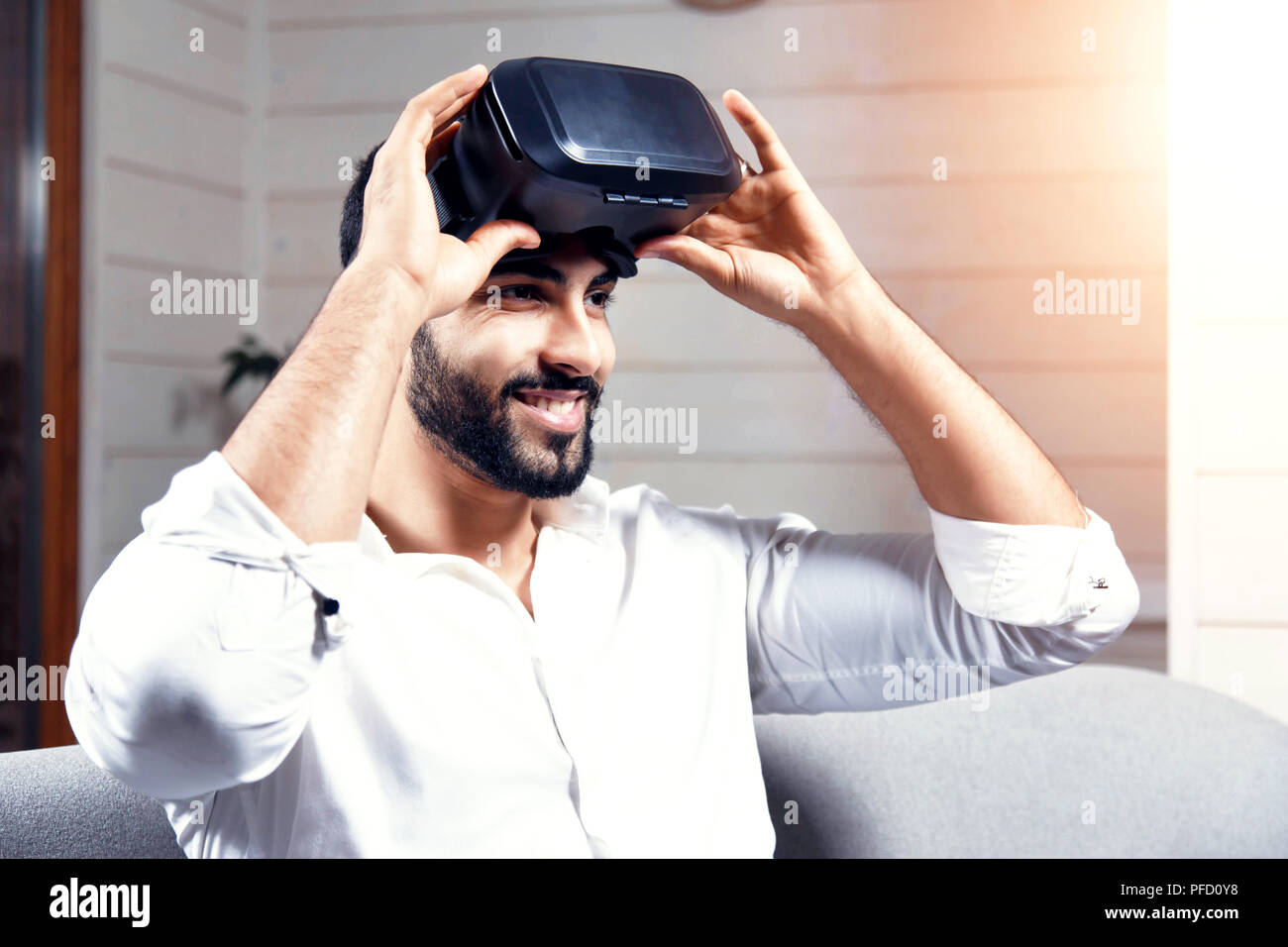 Bel homme arabe noir utilise des lunettes VR set assis sur le canapé en home studio Banque D'Images
