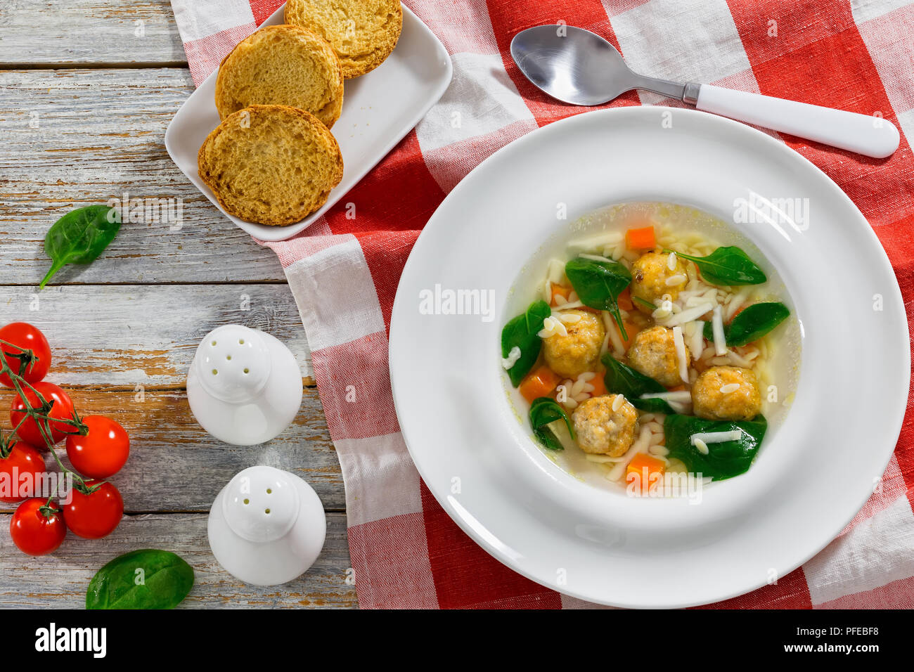 Soupe de noces italiennes avec des boulettes de viande dans la cuvette large blanc sur tapis de table, salière et poivrière, crostini, frais vert d'Épinards et tomates Banque D'Images