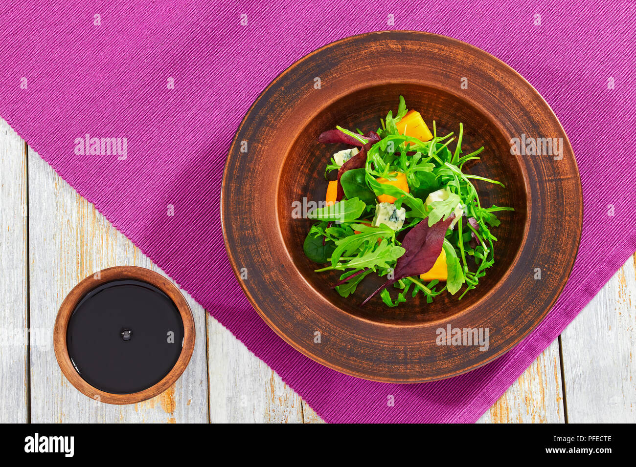 Kaki, fromage bleu, roquette, jeunes épinards, laitue et noix délicieuse salade dans la plaque d'argile avec vinaigrette au vinaigre balsamique sur fond de bois Banque D'Images