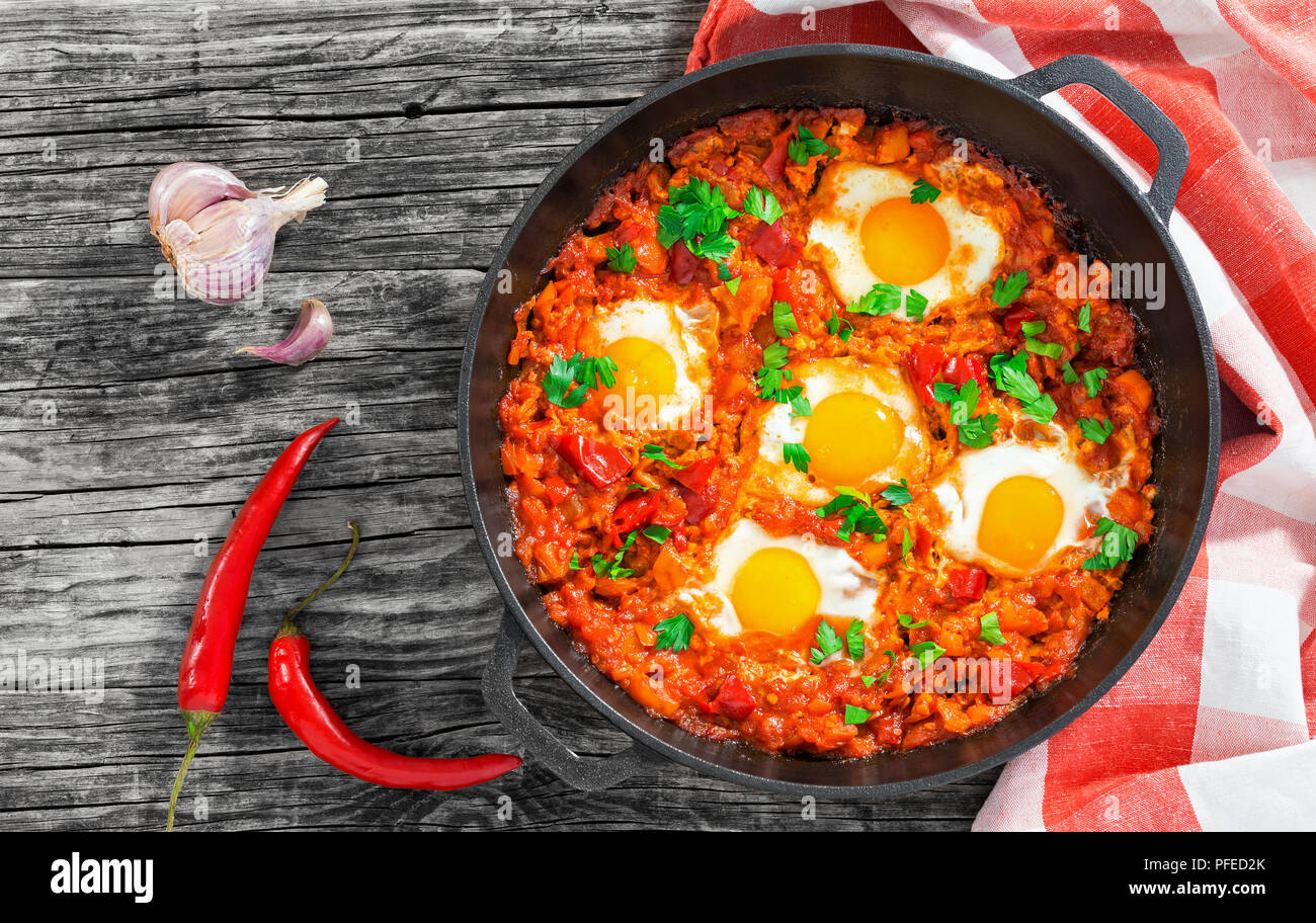 - Shakshuka délicieux œufs frits, oignon, poivron, tomate, piment et épices en cuisine avec poêle en fonte serviette sur planches en bois, authentique destinat Banque D'Images