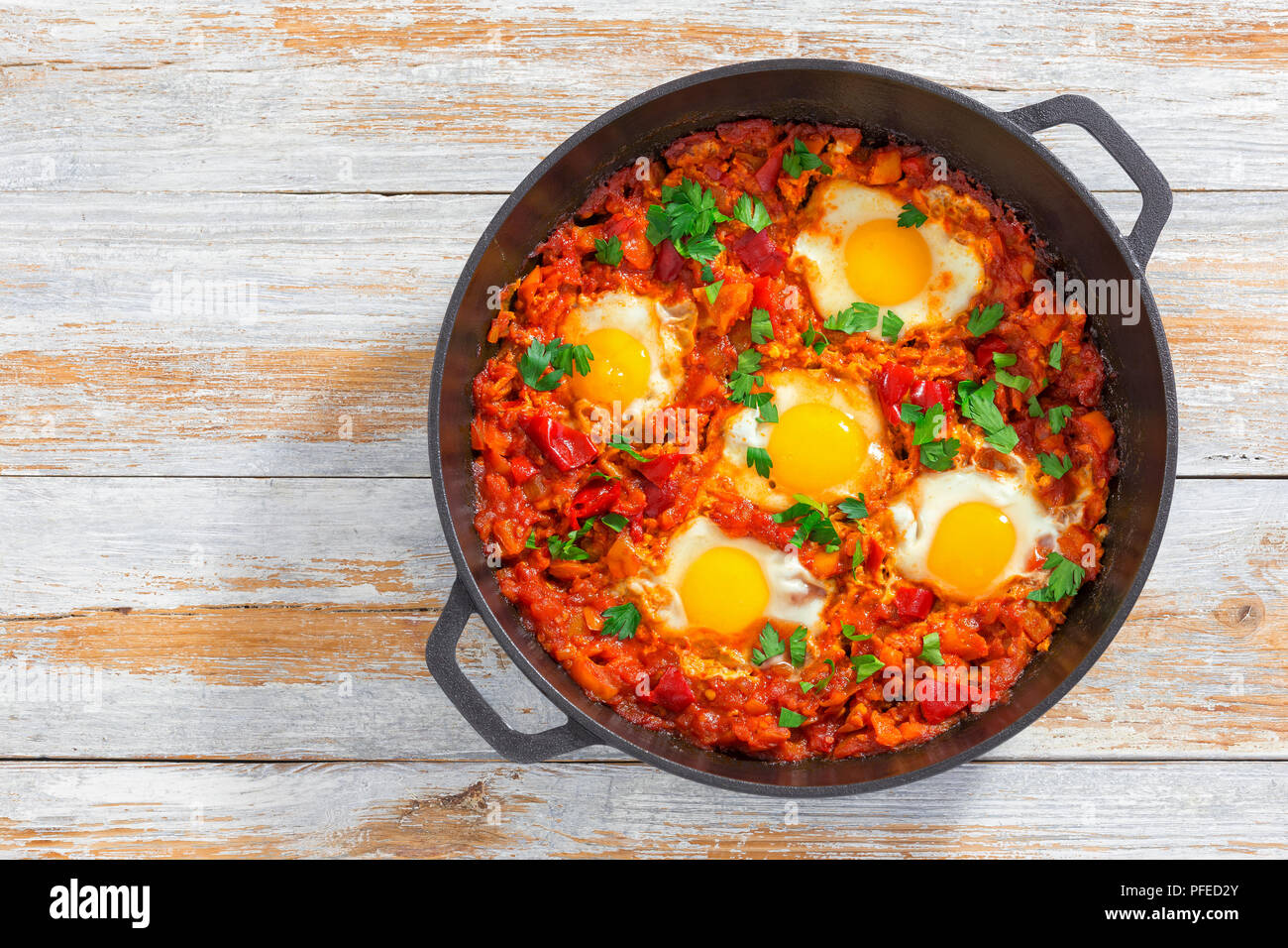 Petit-déjeuner sain shakshuka - œufs, l'oignon, le poivron, les tomates et les épices dans la cocotte en fonte sur le vieux fond de bois, recette authentique, vie Banque D'Images