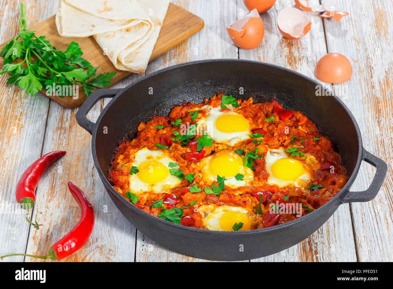 Délicieux moyen-orient shakshuka de base - les œufs, l'oignon, le poivron, les tomates, le piment et les épices dans vieux poêle en fonte sur fond de bois avec elle Banque D'Images