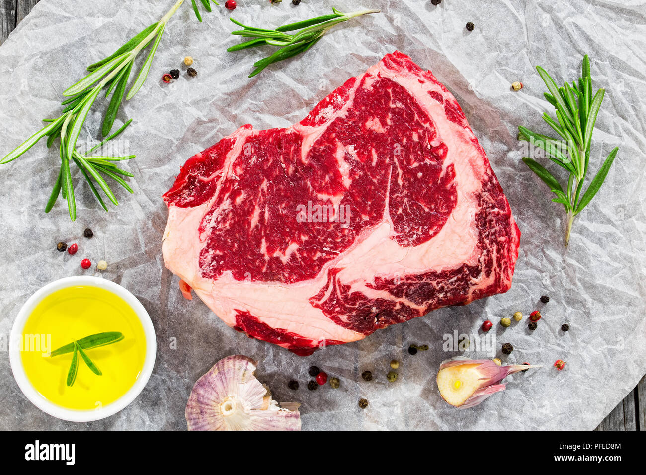 Faux-filet de boeuf steak de viande fraîche sur du papier blanc avec le romarin, l'ail et l'huile d'olive, vue de dessus, close-up Banque D'Images