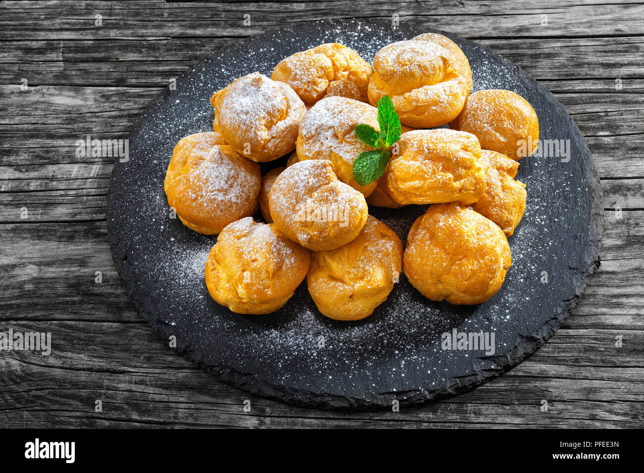 Profiteroles délicieux rempli de crème sur la plaque d'ardoise, de dépoussiérage, de sucre en poudre, sur la vieille table en bois sombre, vue de dessus, close-up Banque D'Images