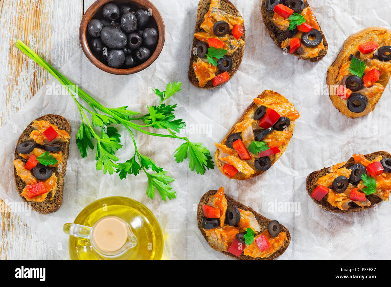 Bruschetta avec un filet de poisson, anneaux d'olive et des morceaux de poivron rouge, sur papier blanc avec l'huile de cuisson et le bol d'olives noires sur la table en bois, vue Banque D'Images