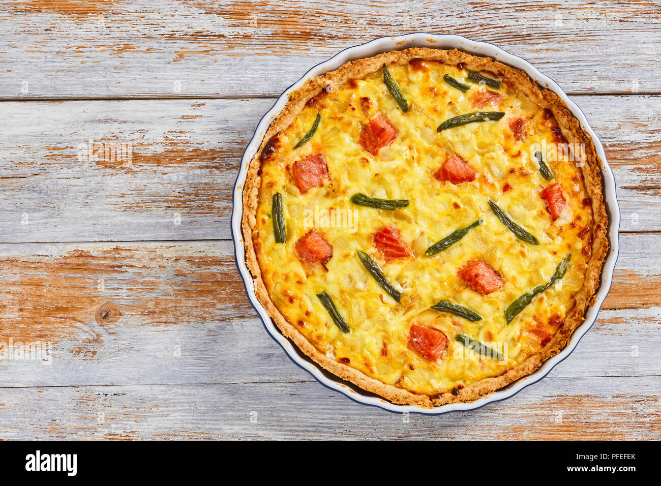 Tarte quiche délicieux saumon farci aux haricots verts,et l'Emmental, la crème, l'oignon et les œufs dans le plat de cuisson sur la vieille table en bois blanc, vue depuis l'ab Banque D'Images