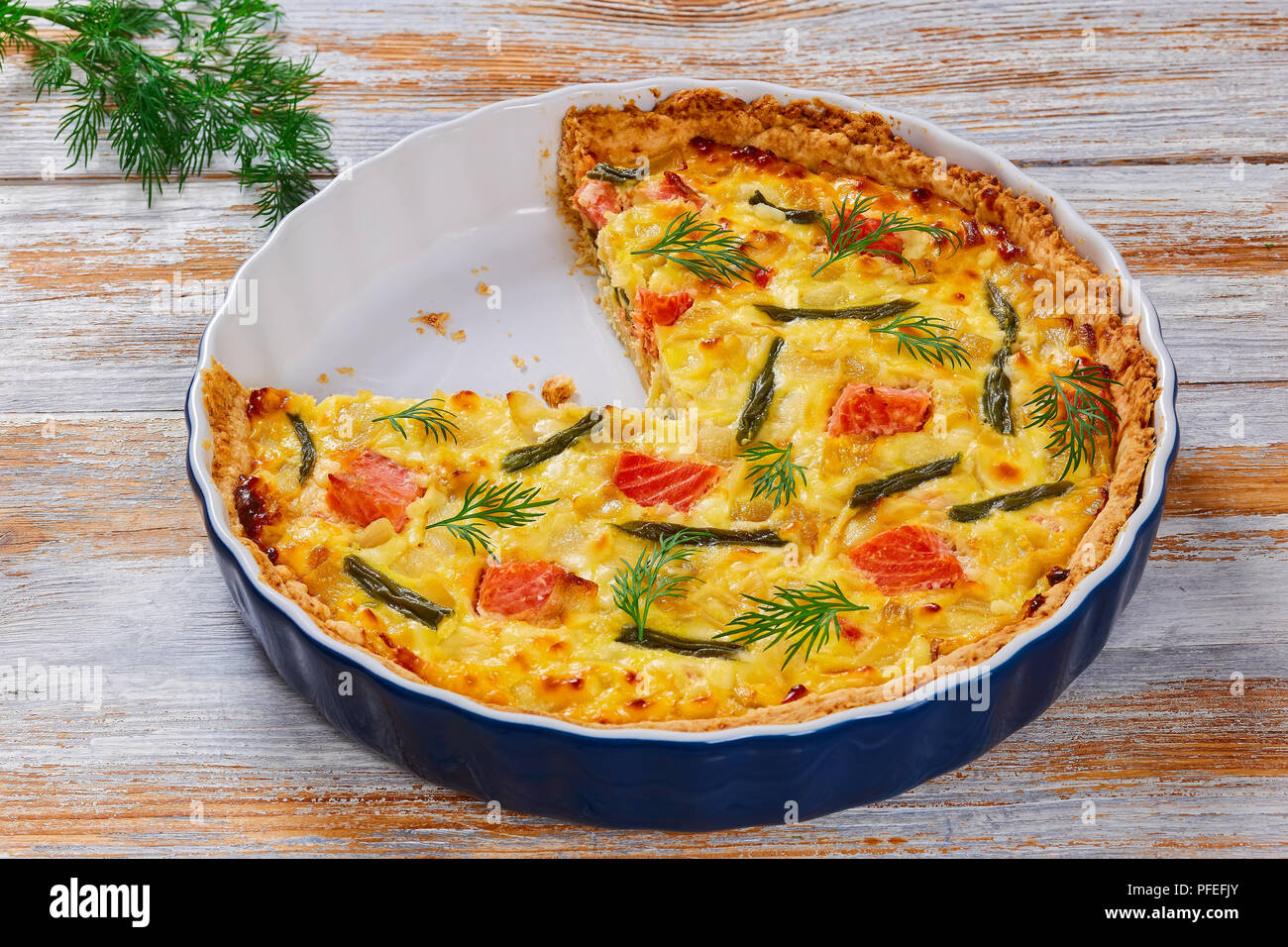 Quiche au saumon, haricot vert et l'Emmental, la crème, l'oignon et les œufs avec de l'aneth coupé en tranches dans le plat de cuisson sur table rustique blanc, vue Banque D'Images