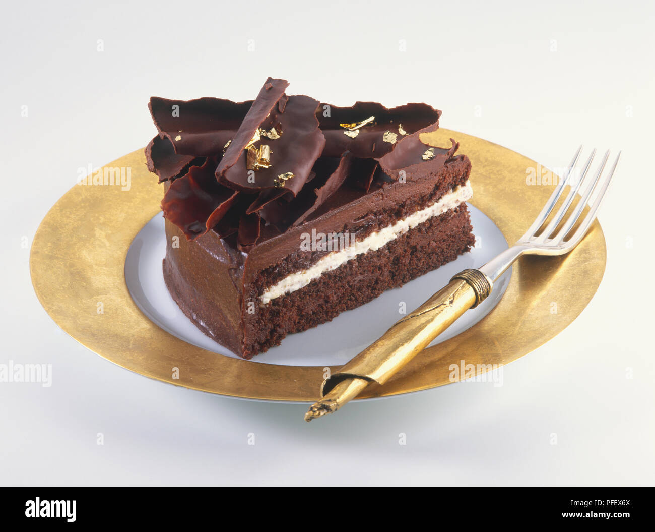Tranche De Gateau Au Chocolat Decore De Copeaux De Chocolat Et Des Morceaux De Feuilles D Or Servi Sur La Plaque D Or Avec La Fourche D Or Side View Photo Stock Alamy