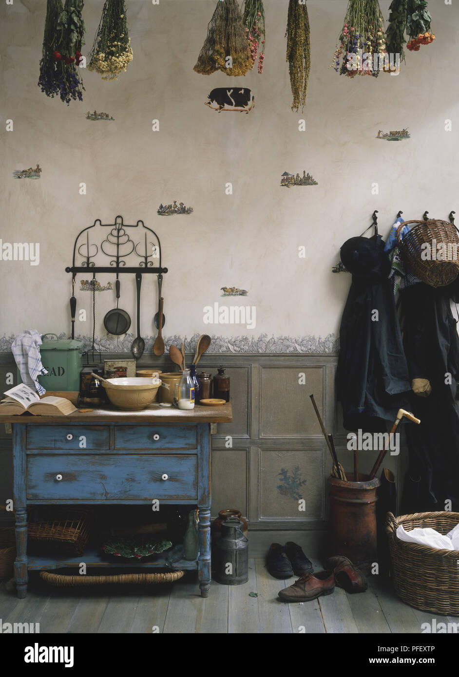 Une salle rustique contenant des ustensiles de cuisine sur un tableau bleu, les plantes séchées qui pendait au plafond, manteaux sur des crochets sur le mur, panier en osier et des chaussures sur marbre Banque D'Images
