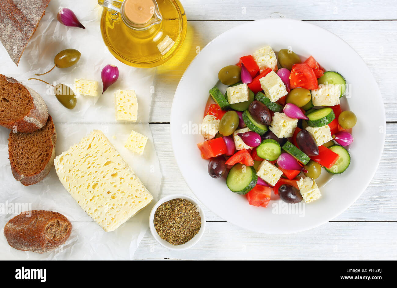 Délicieuse salade grecque avec des légumes frais, fromage feta et olives de Kalamata vert, oignon rouge ampoules sur plaque blanche sur table avec pain de campagne croustillant Banque D'Images