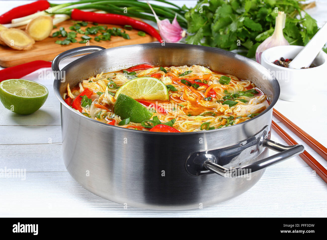 Poulet Thaï au curry vert et épais pour la soupe de nouilles au lait de coco, légumes et herbes dans la casserole sur la table en bois avec des ingrédients sur Banque D'Images