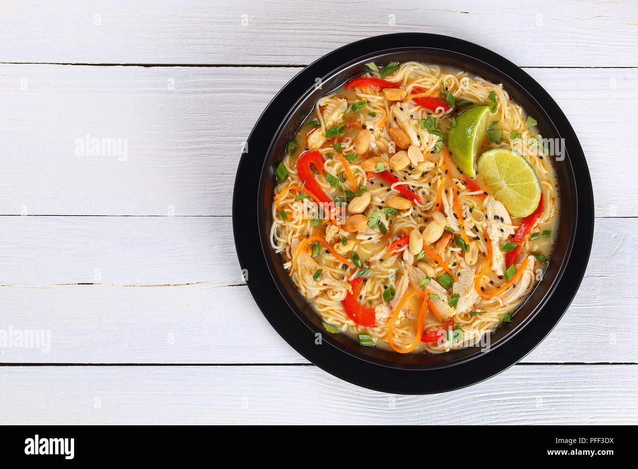Pâte de curry vert de poulet thaï au lait de coco, légumes et fines herbes dans un bol noir parsemé de graines de sésame et d'arachide sur travail en bois Banque D'Images