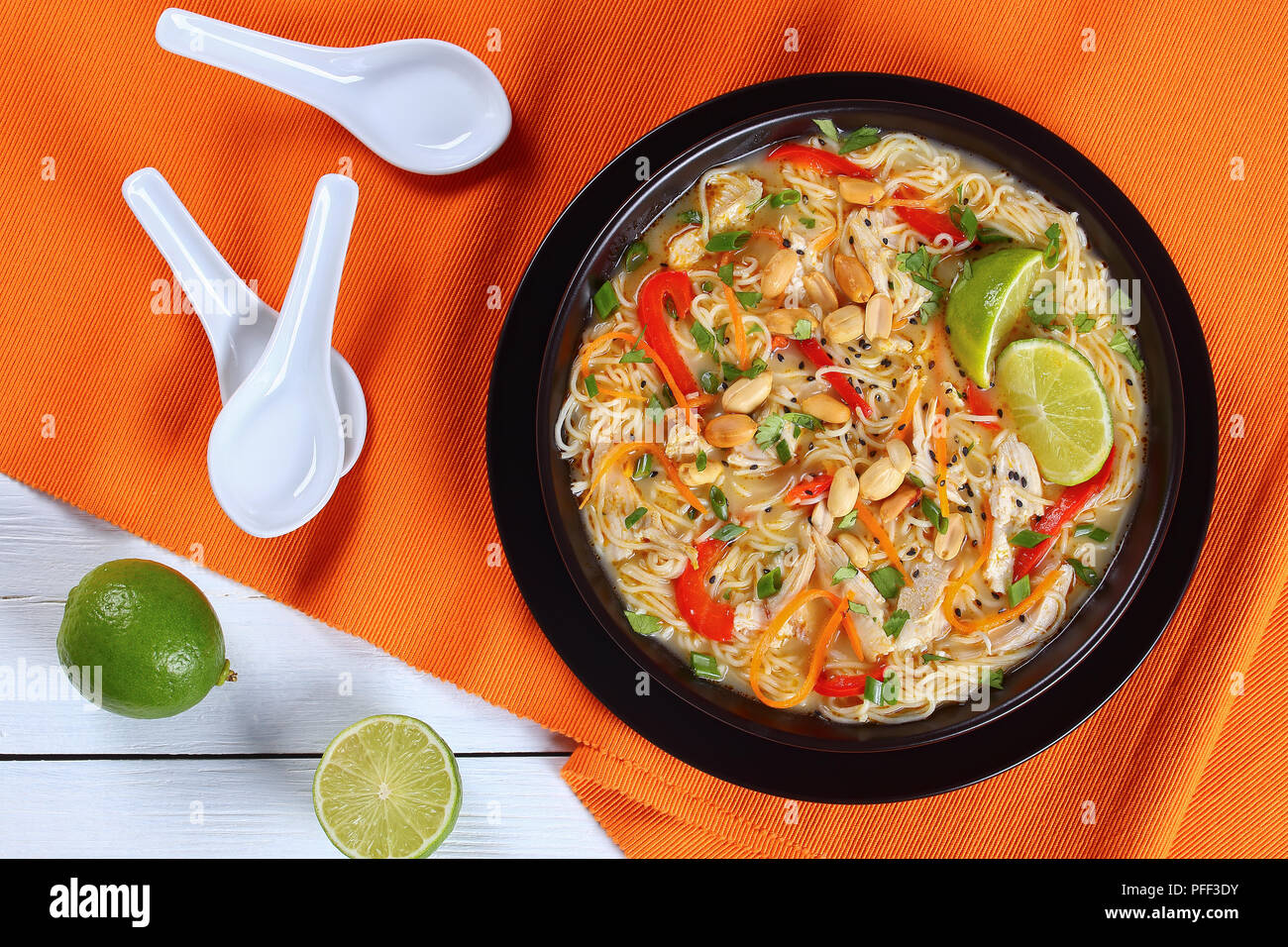Pâte de curry vert de poulet thaï au lait de coco, légumes et fines herbes dans un bol noir parsemé de graines de sésame et d'arachide sur travail en bois Banque D'Images