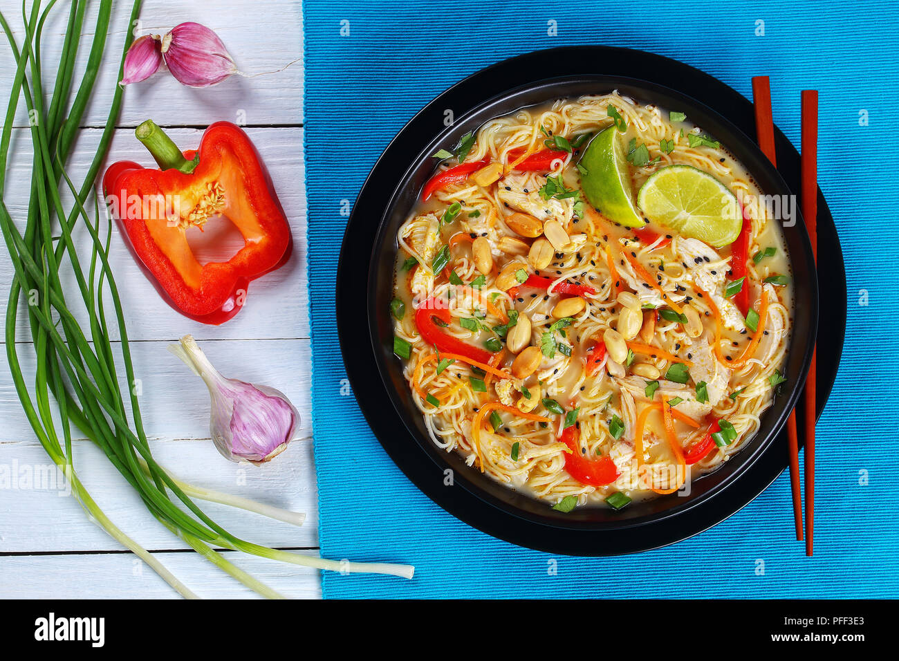 Soupe Poulet et nouilles thaï saupoudré de coriandre, de sésame et d'arachide dans un bol avec des baguettes noires. l'oignon vert, la moitié de poivron rouge et g Banque D'Images