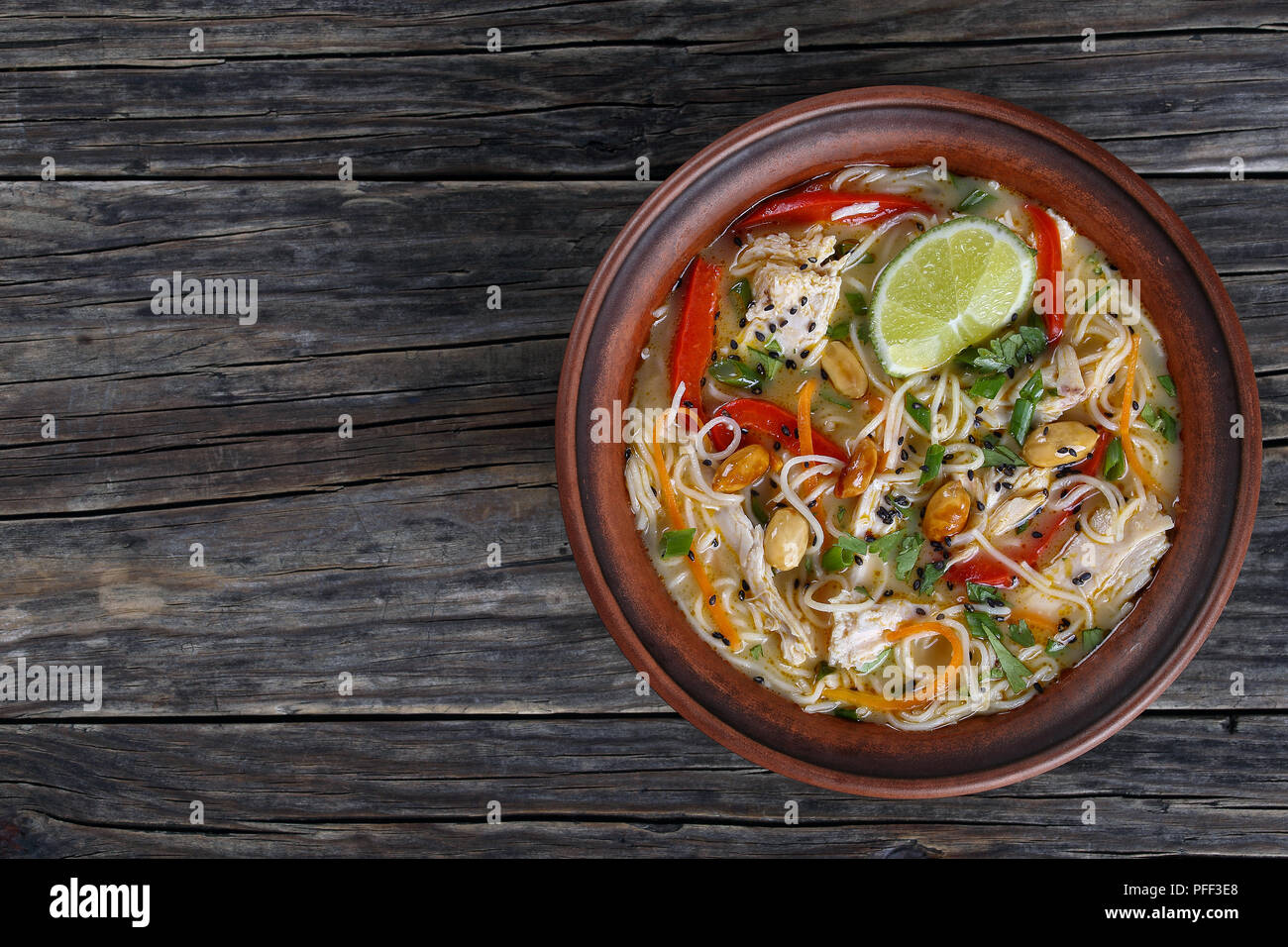 Soupe Poulet et nouilles thaï délicieux saupoudré de sésame noir, finement hachées coriandre, arachides et décorée avec une lime slices en cuvette d'argile, vue à partir de Banque D'Images