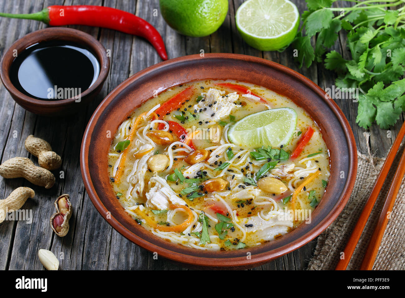 Soupe Poulet et nouilles asiatiques parsemés de sésame, la coriandre finement hachée, d'arachides et décorée avec une lime slices en cuvette d'argile, de la sauce de soja chili pepp Banque D'Images
