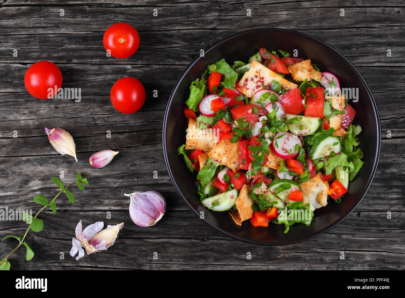 Délicieux pain libanais ou Fattoush salade avec des croûtons de pain pita, le concombre, la tomate, la laitue et les fines herbes dans un bol sur une table en bois noir, authent Banque D'Images