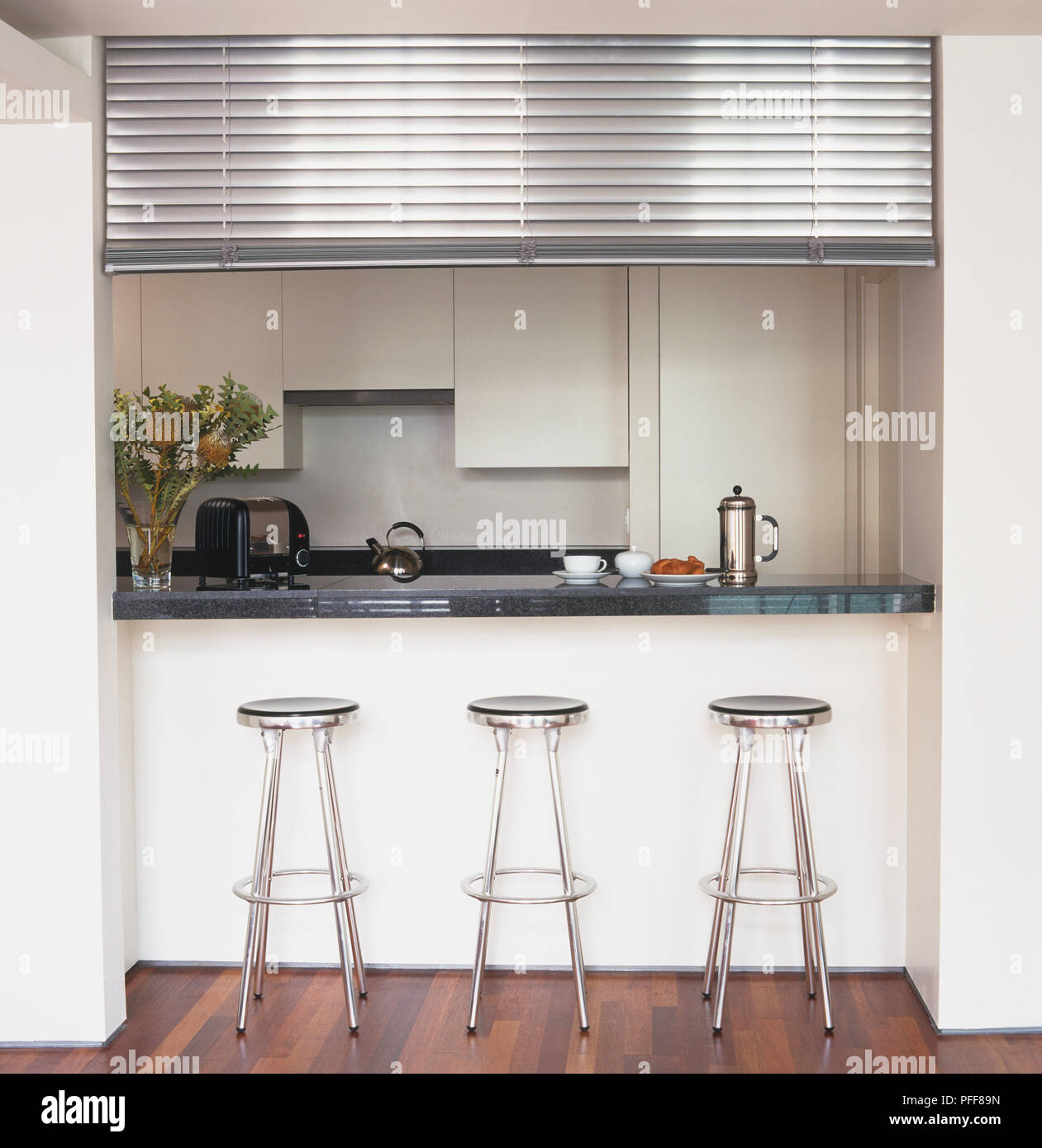 Trois tabourets métalliques alignés par la fenêtre style de restaurant-bar à la recherche en cuisine, stores partiellement repliée au-dessus. Banque D'Images