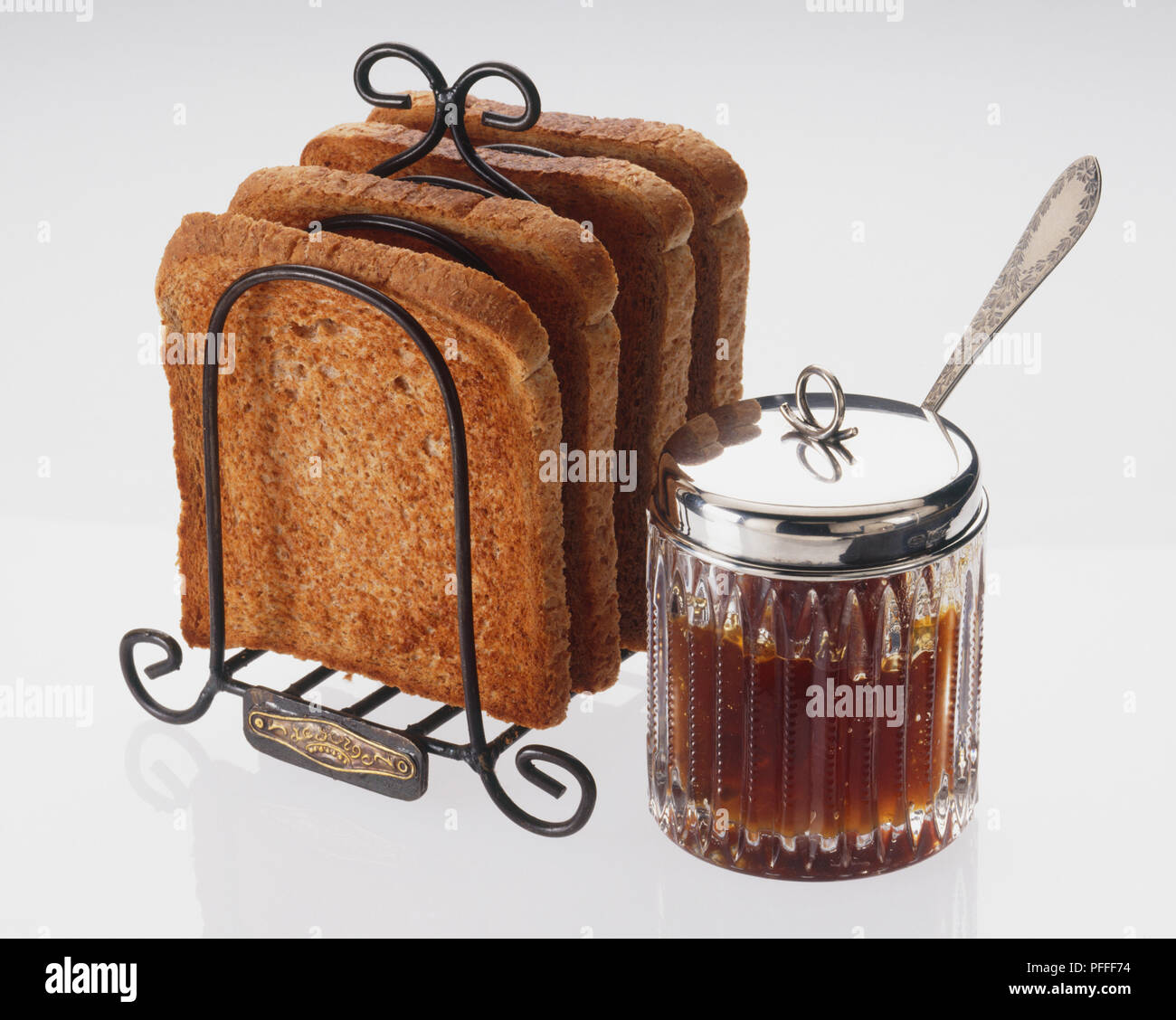 Jam servi dans un bocal en verre avec un couvercle d'argent et une cuillère, et un toast rack contenant quatre tranches de pain grillé Banque D'Images