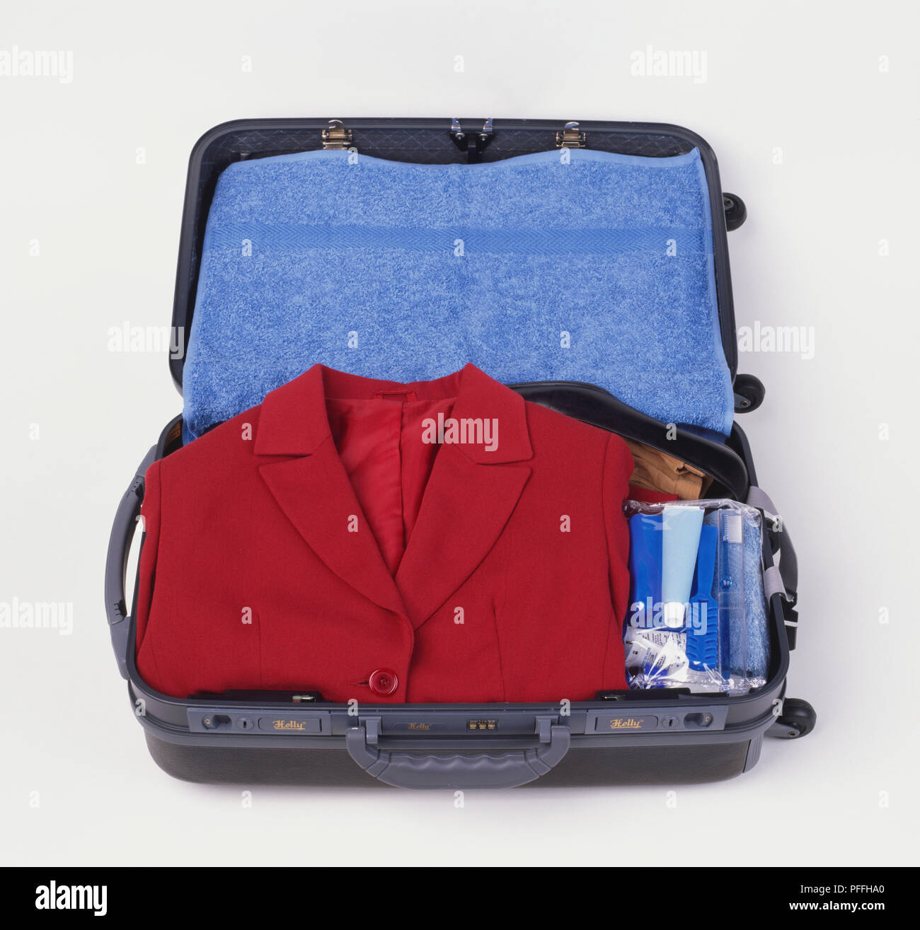 Valise contenant une veste rouge soigneusement plié, une serviette bleue et d'autres accessoires. Banque D'Images