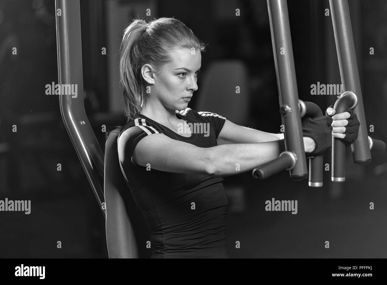 Femme à la salle de sport sport faire des exercices d'armes sur une machine Banque D'Images