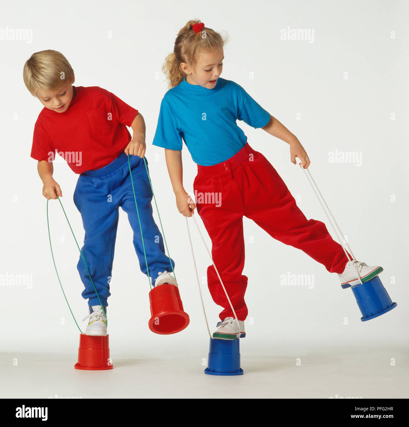 Garçon en équilibre sur deux seaux, pilotis ; rouge et bleu Banque D'Images