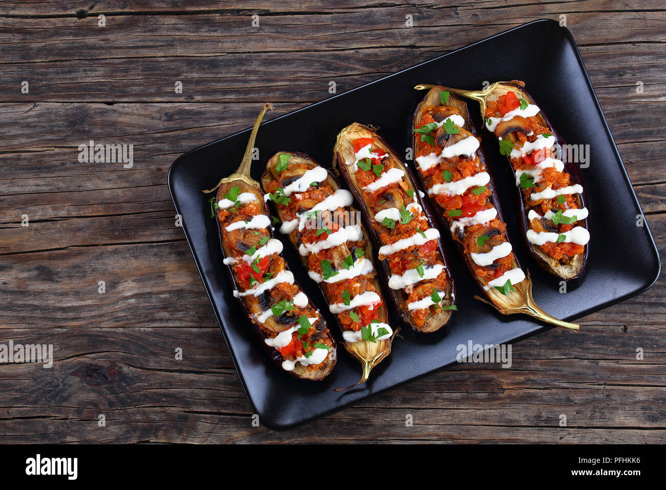 De délicieux champignons Quinoa Aubergines farcies de tomates avec la sauce Tahini sur plaque noire sur la vieille table en bois, facile et recettes santé, vue de dessus, c Banque D'Images