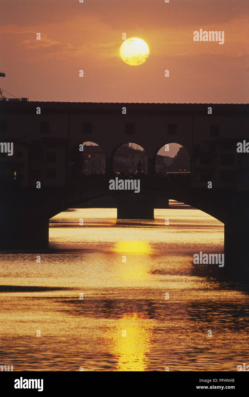 Italie, Florence, Ponte Vecchio, coucher de soleil rougeoyant au-dessus du pont et se reflétant dans la rivière Arno Banque D'Images