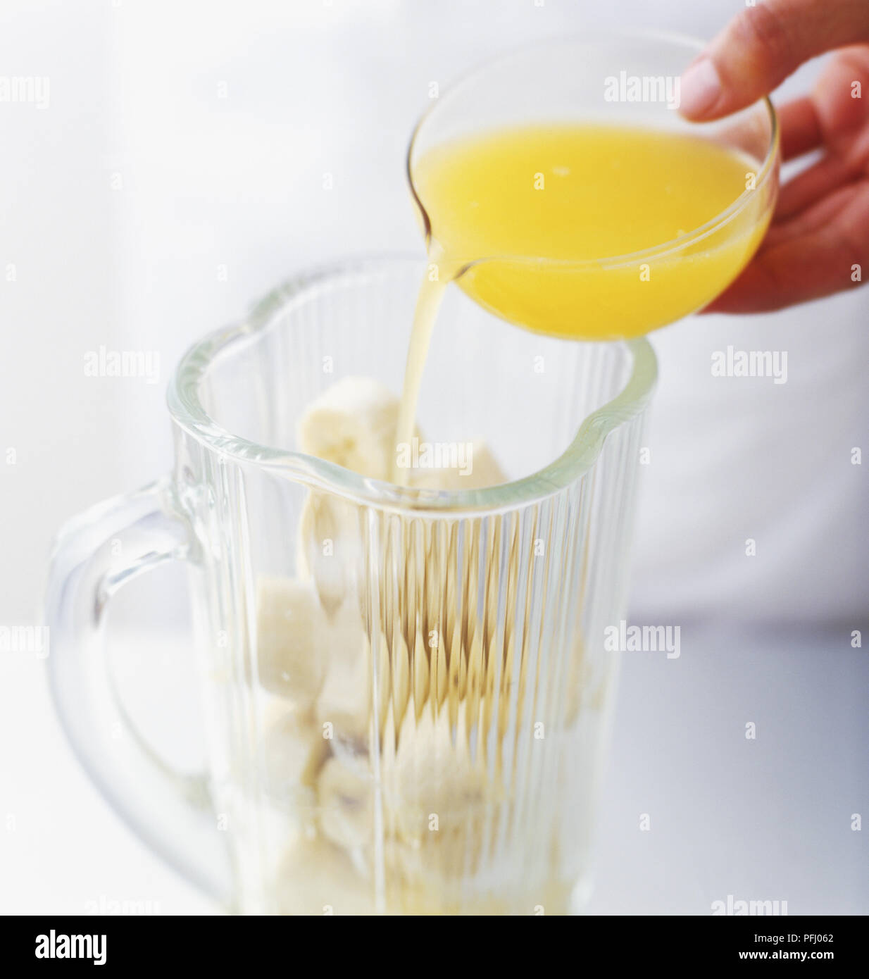Verser le mélange de jus de citron et d'orange sur la banane dans un mélangeur Banque D'Images
