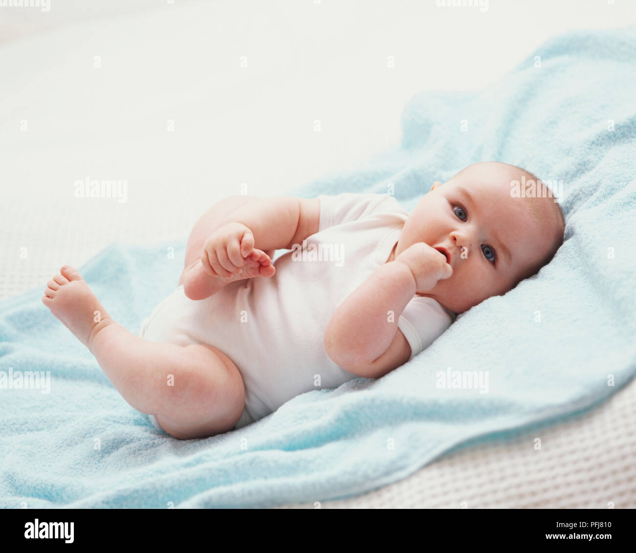 Ronchonnant Pied de bébé avec une main, tout en mettant le poing dans la bouche avec l'autre Banque D'Images