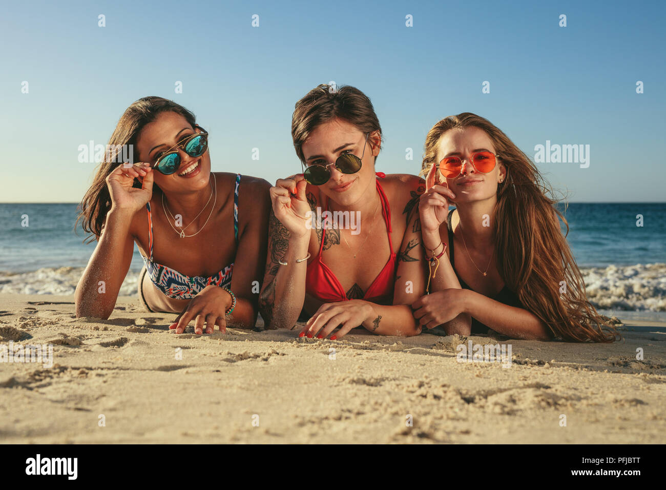 Trois femmes en bikini allongée sur un bain de soleil sur la plage avant  tenant leurs lunettes de soleil. Femme en vacances de détente à la plage le  port de lunettes havi