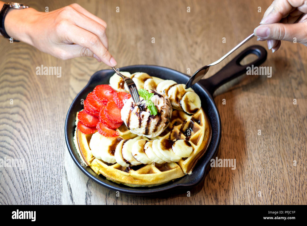 Main tenant manger fourche gaufre avec de la glace à la vanille et des fruits frais dans un restaurant table Banque D'Images