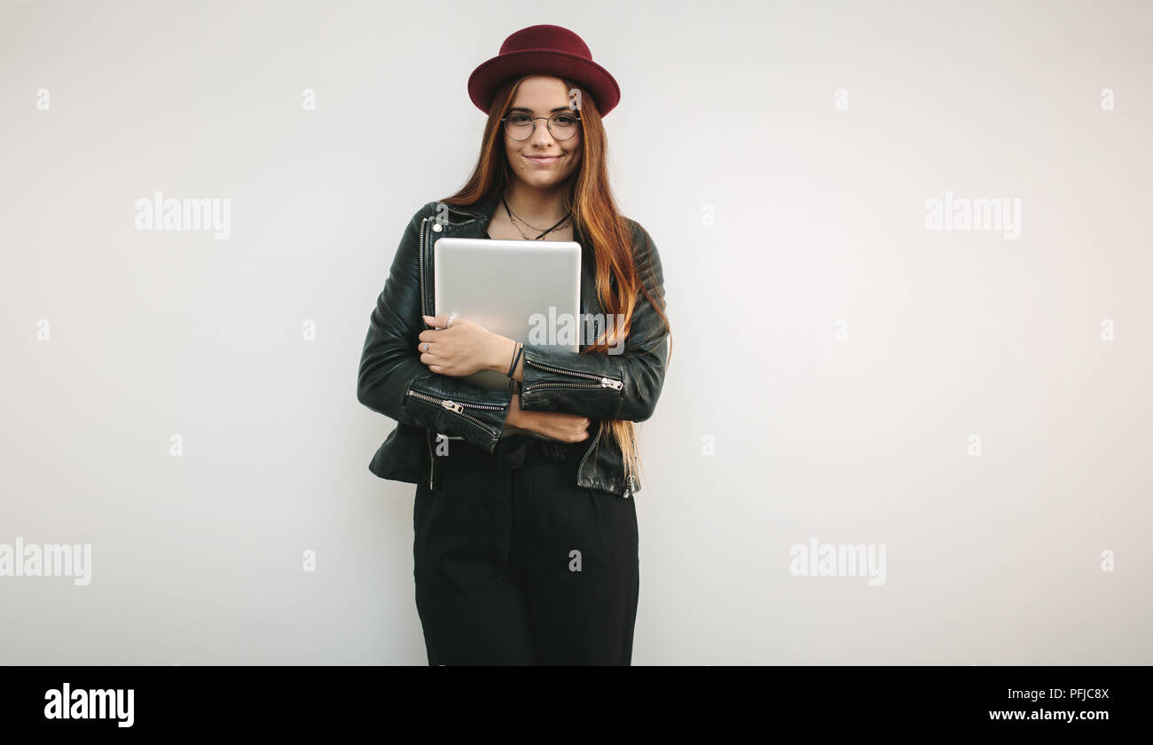 Portrait d'une femme portant des lunettes et un chapeau tenant un ordinateur portable. Smiling woman holding avec bras croisés. Banque D'Images