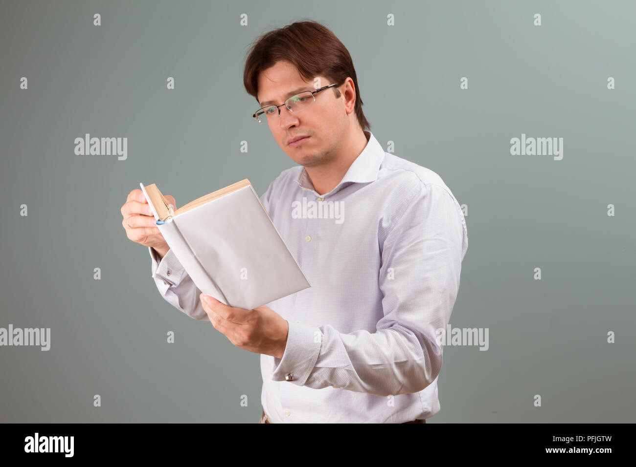 Un jeune homme porté sur la lecture d'un livre à couverture blanche ; l'orientation horizontale portrait studio. Banque D'Images