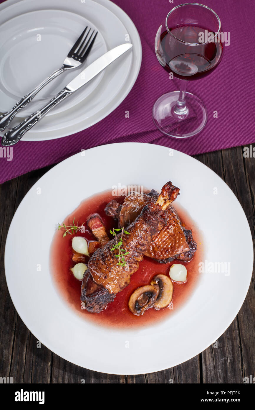 Partie de ragoût de poulet - braisé de cuisse et le pilon avec vin, lardons, champignons et herbes servi sur plaque avec verre de vin rouge, d'authentiques français Banque D'Images