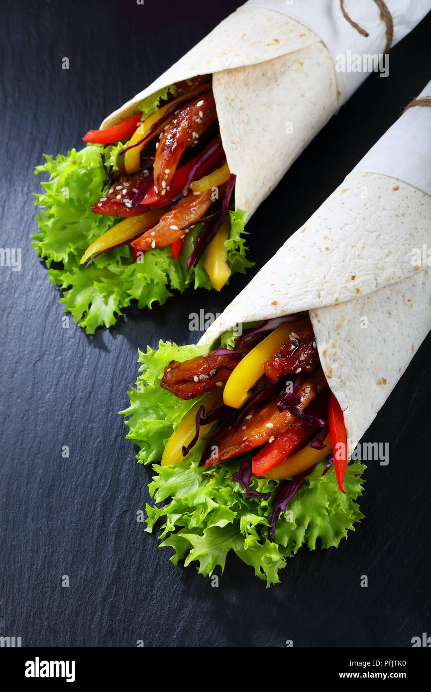 Tortilla enroulée autour d'un remplissage - salade de chou rouge, le poivron doux et fried chicken viandes sur ardoise noire bac, sur une table en bois, vue de abov Banque D'Images